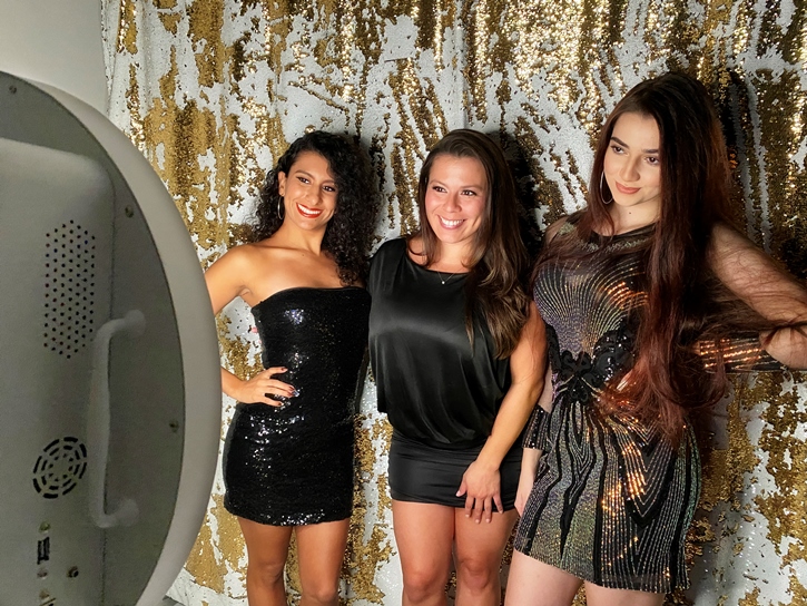 Women taking a picture with photo booth and gold photo booth backdrop