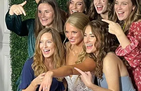 A bride and her friends pose before a photo booth backdrop during a wedding